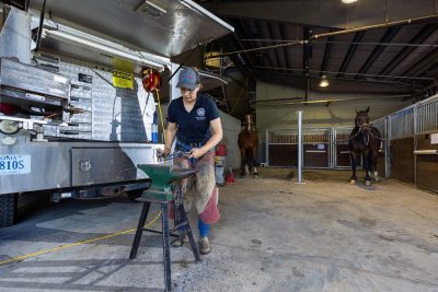 Victoria Protasenko working on a horse shoe beside a farrier truck.