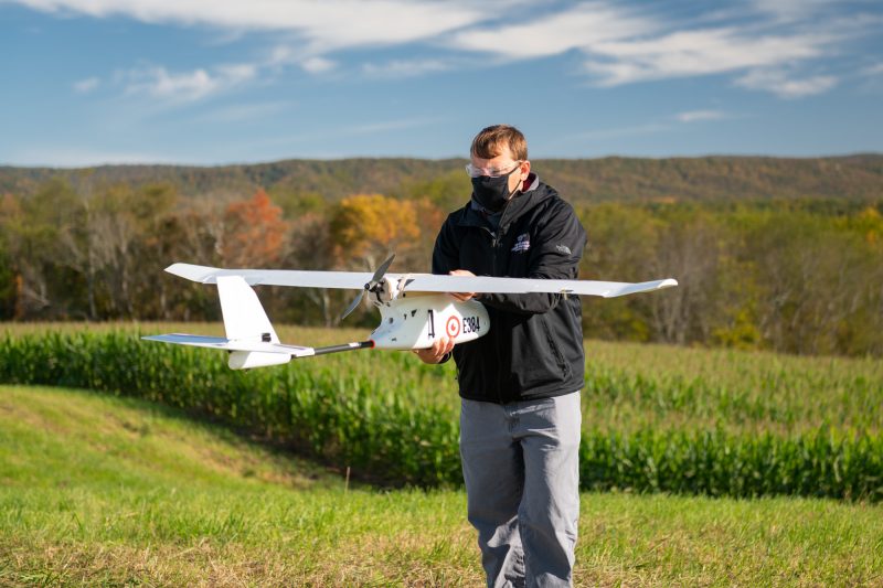 An engineer prepares a fixed-wing drone for flight in a rural area